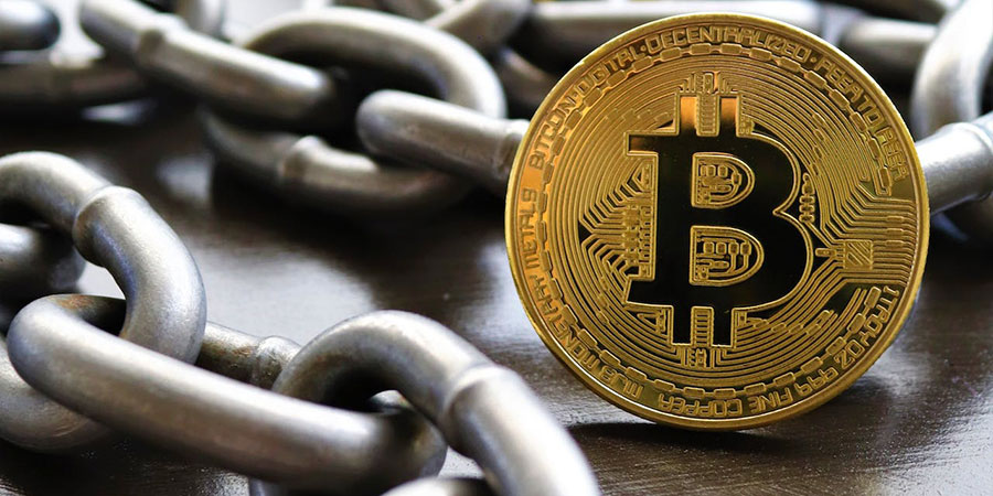 close up view of a gold Bitcoin and a metal chain on top of a wooden surface