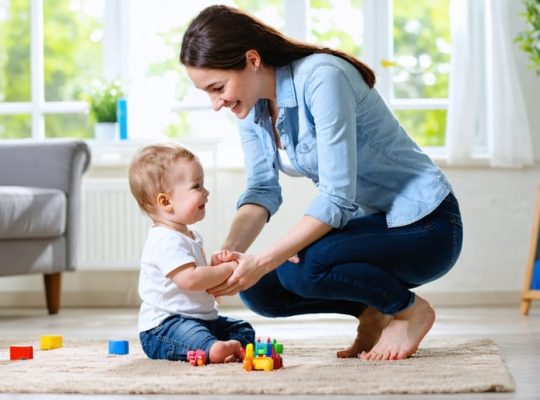 Parent kneeling and smiling while making eye contact with their child, emphasizing supportive and nurturing interaction in a home setting.