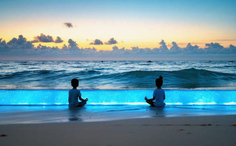 Silhouettes of children practicing meditation at sunrise on a beach, surrounded by gentle blue ocean waves with a subtle blue glow, symbolizing the calming effect of blue light meditation.