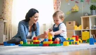 Parent and child sitting on the floor in a brightly lit playroom, engaged in a playful activity with colorful building blocks, symbolizing the nurturing bond formed through therapeutic play.