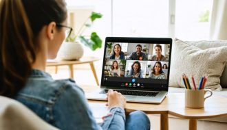 A mother taking notes as she participates in a virtual parenting class on a laptop from her living room, with other diverse parents visible on the screen in a supportive video conference.