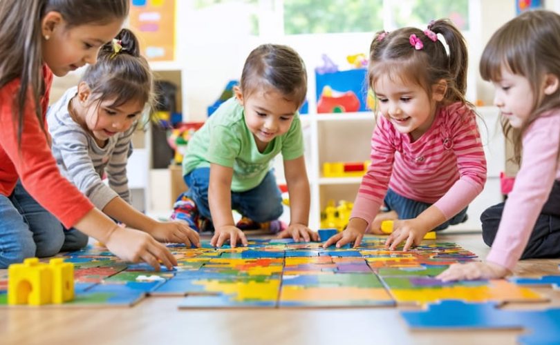 A diverse group of children happily collaborating on assembling a large puzzle on the floor, demonstrating teamwork and communication in a playful setting.